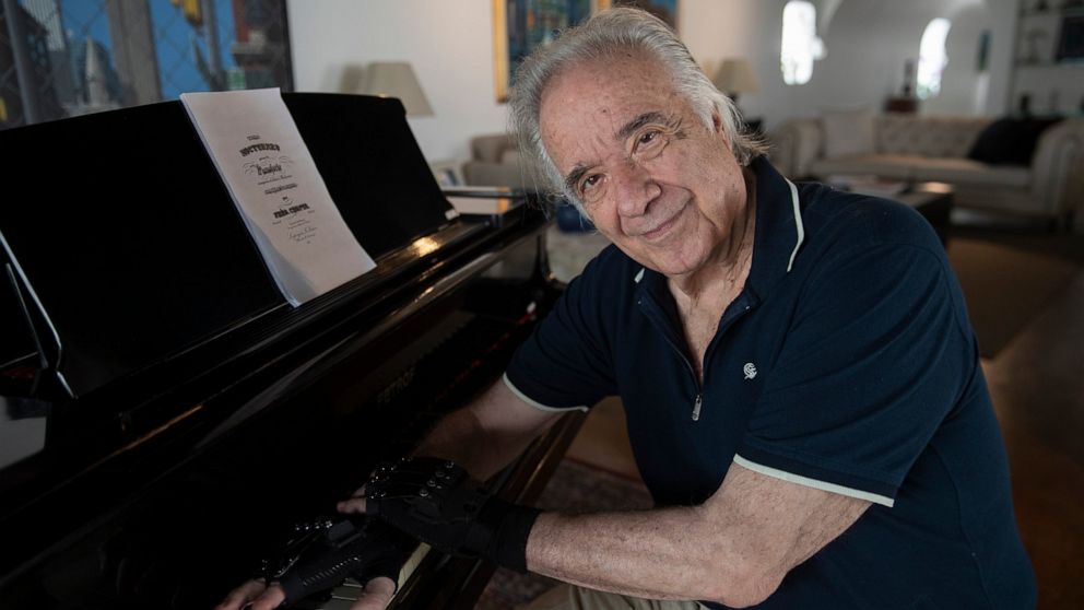 Brazilian pianist Joao Carlos Martins poses for pictures wearing bionic gloves, at his home in Sao Paulo, Brazil, Wednesday, Jan. 22, 2020. Martins, 79, was for decades Brazil's most acclaimed pianist, but an accident an a degenerative disease forced
